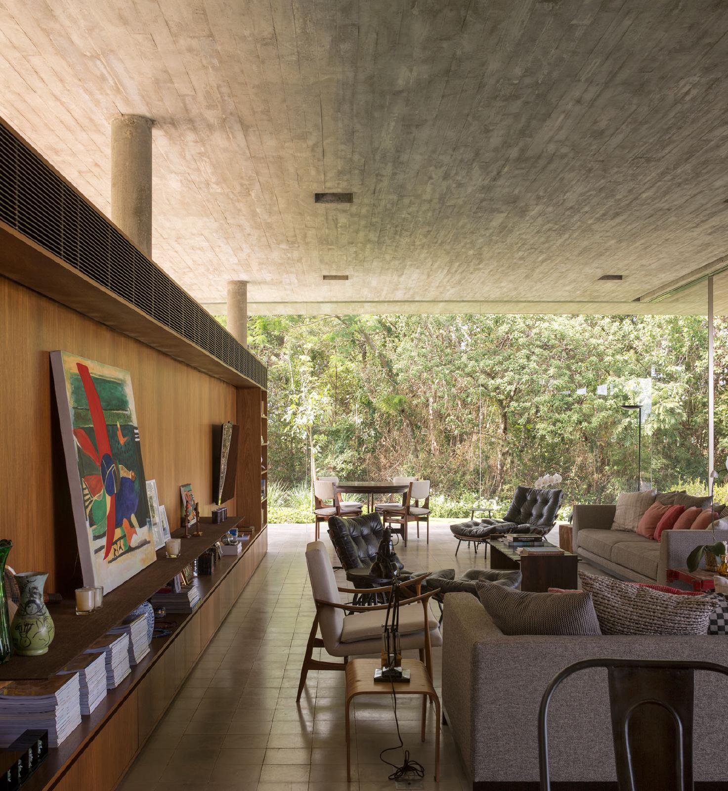 Sala aberta ao jardim, com teto de concreto e mobiliário de madeira